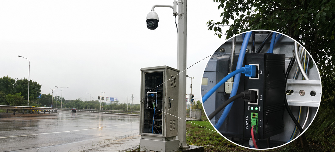 Real-world highway roadside field deployment of Benchu Group industrial PoE++ injector inside an open metal telecommunication cabinet powering a high-draw outdoor PTZ surveillance camera on a pole during wet rainy weather conditions.